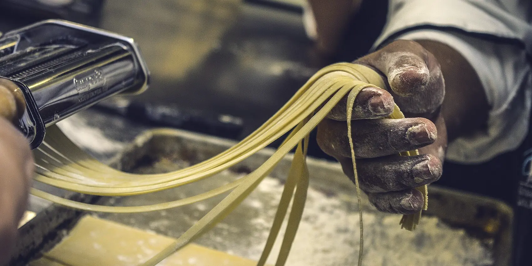 Mani infarinate raccolgono i tagliolini che escono dalla macchina della pasta.