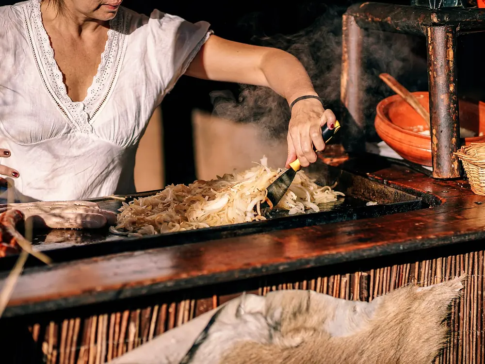 Marta rigira le verdure sulla piastra rovente, avvolta dal vapore.