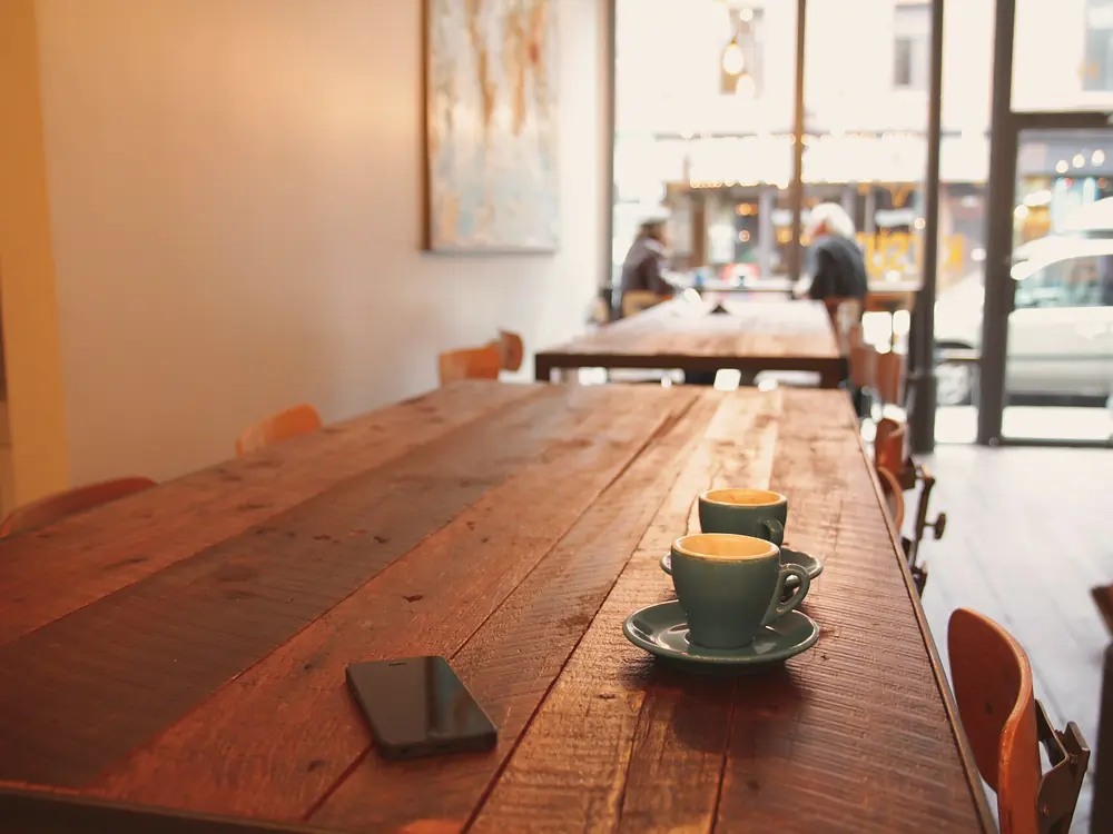 Il lungo tavolo di legno della sala, apparecchiato e illuminato dalla luce della vetrina.