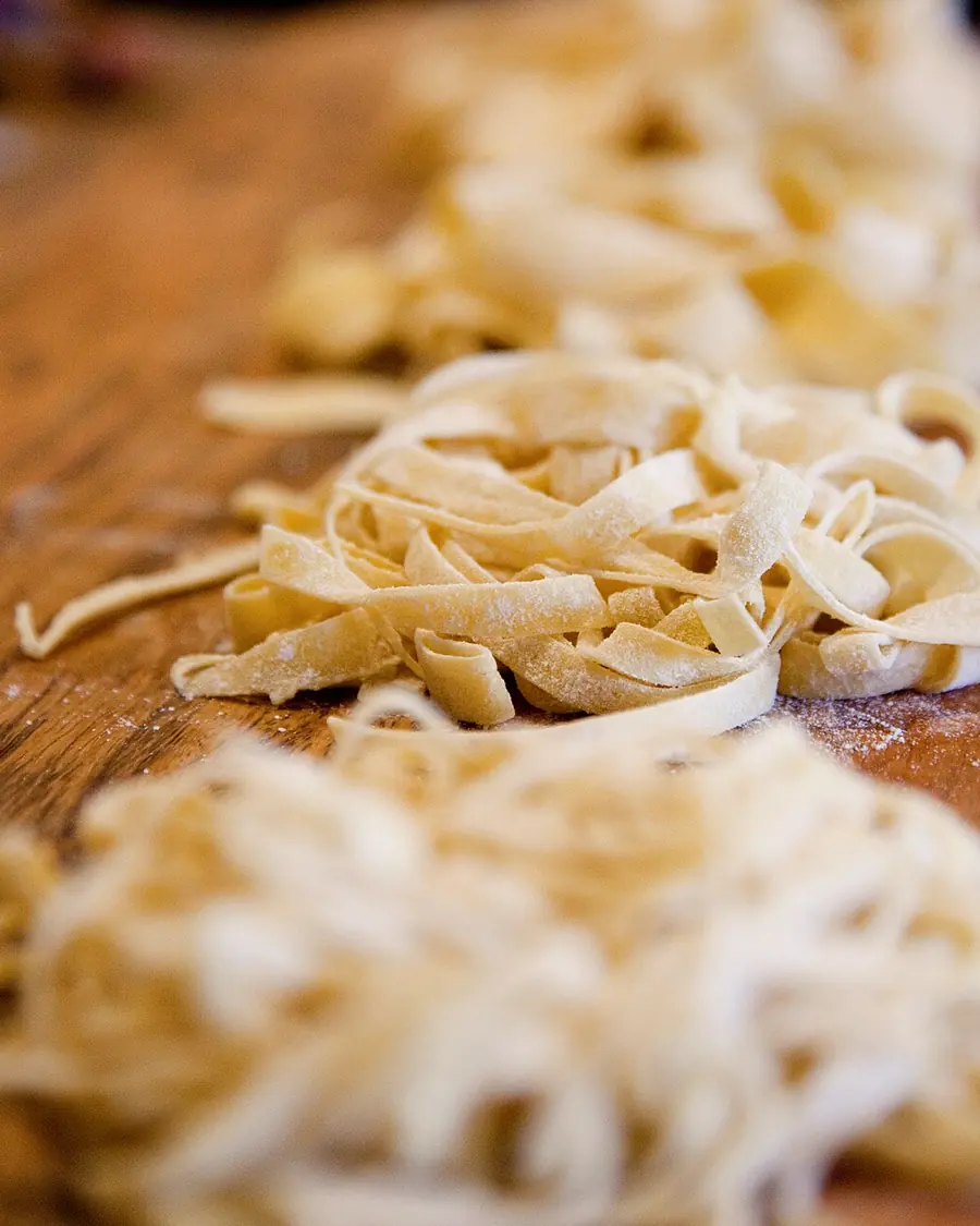 Nidi di tagliatelle fresche appena tagliate, posati su un tavolo di legno infarinato.